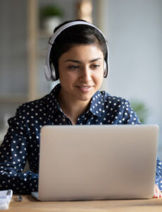 Millennial Indian Girl In Headphones Using Laptop At Home